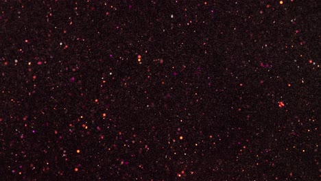 in slow motion, pink and gold glitter particles move almost randomly against a black background
