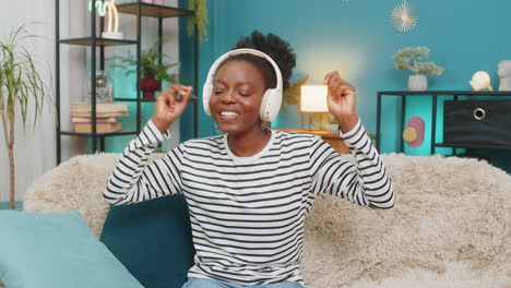 african american woman girl enjoying listening music dancing on sofa wireless headphones at home