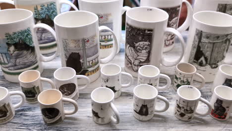 assorted ceramic mugs with cat illustrations displayed on a wooden surface