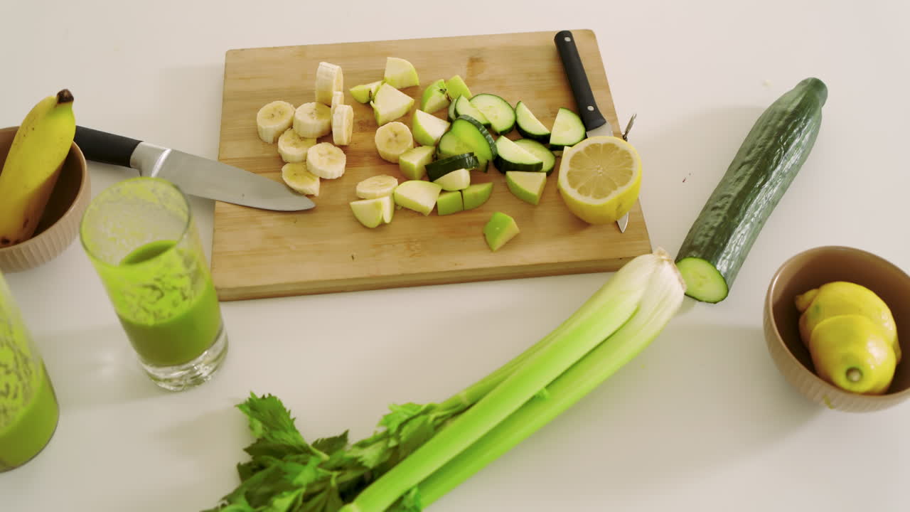 Preparazione di un frullato verde salutare con frutta e verdura fresca sul piano di lavoro della cucina.