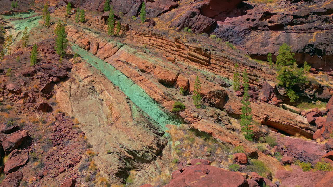 Luftfoto af de farverige vulkanske klippeformationer ved Los Azulejos de Veneguera, med unikke grønne og røde minerallag på Gran Canaria.