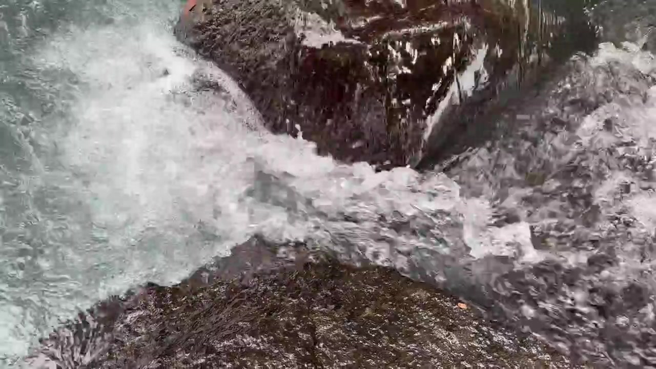 Acqua limpida che scorre impetuosa e si infrange su rocce scure