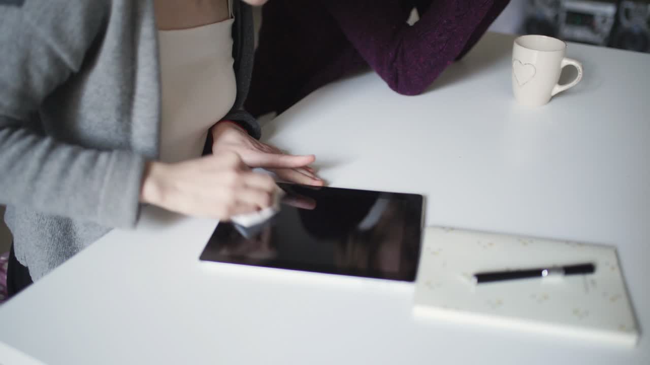 Female hands wiping surface screen tablet pc with cloth lying on table