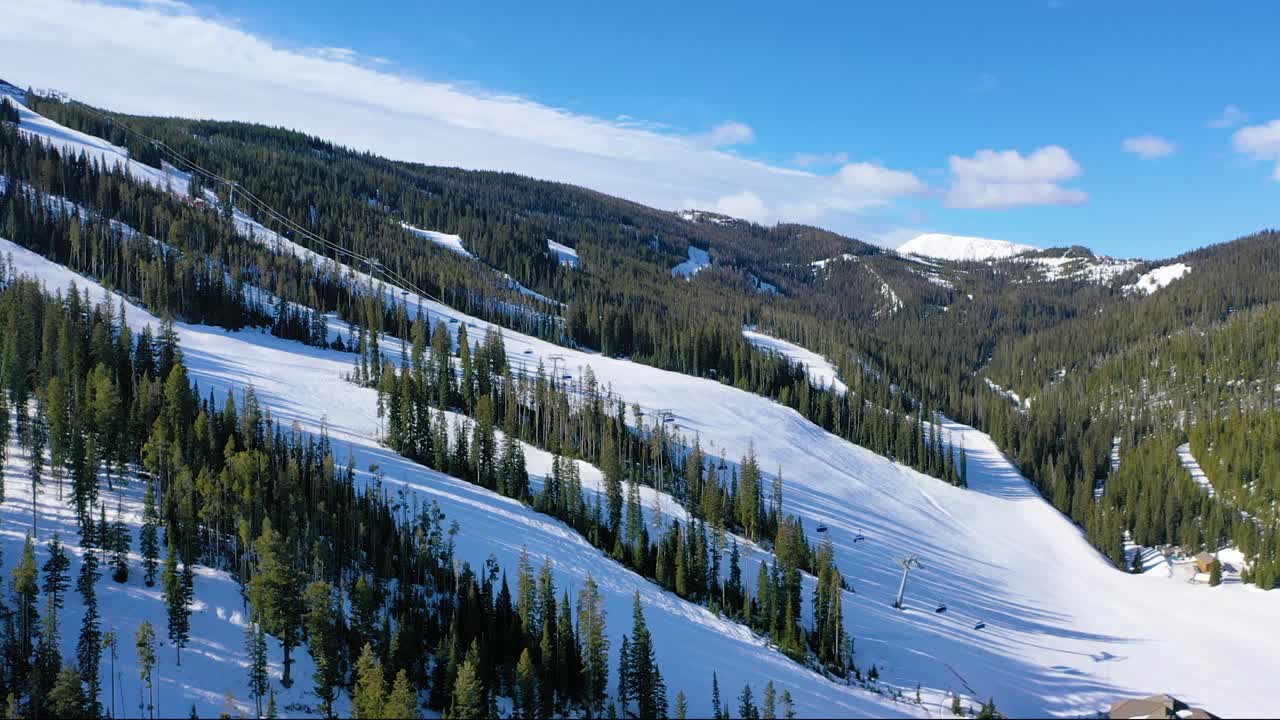Winter drone footage of Big Sky shows skiers riding lifts and flying down trails, with pine forests and snow-packed mountain terrain completing the stunning alpine view