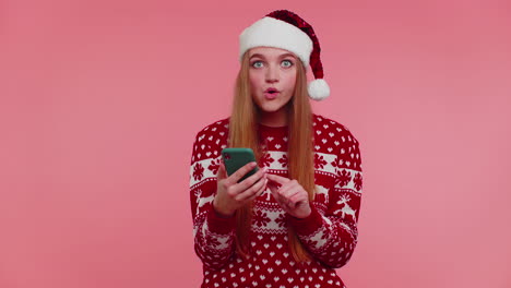 Erwachsenes-Mädchen-Im-Weihnachtspullover-Schaut-Auf-Smartphone-Display-Und-Freut-Sich-Aufrichtig-über-Erfolg-Und-Glück