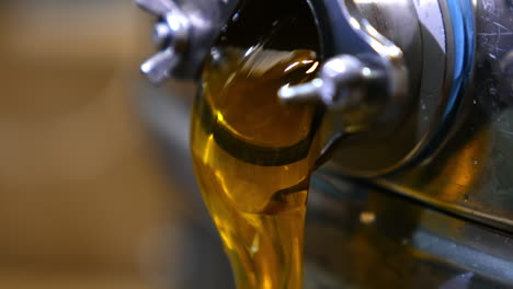 honey extracted from frames in the electric device flowing from faucet. close up. organic product leaking out of machine.