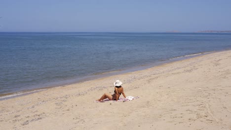 Young-woman-in-bikini-sitting-on-sandy-beach