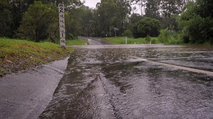 Gold Coast, Queensland, 16 February 2024 - Low shot of waterflow into flooding across Hardy's Road in Mudgeeraba after heavy rains continue to lash South East Queensland, Australia