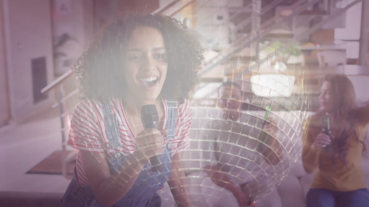 Composite of happy friends singing karaoke and drinking beers at home, and mirrorball