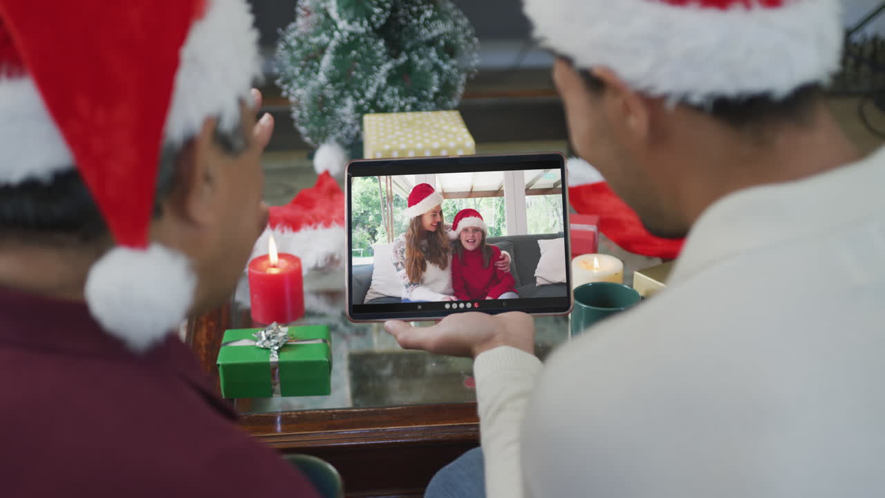 padre biracial con hijo agitando y usando la tableta para la videollamada de navidad con la familia en la pantalla
