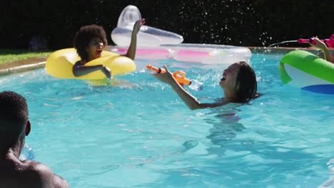 Vielfältige-Gruppe-Von-Freunden,-Die-Spaß-Daran-Haben,-Mit-Wasserpistolen-Auf-Schlauchbooten-Im-Schwimmbad-Zu-Spielen