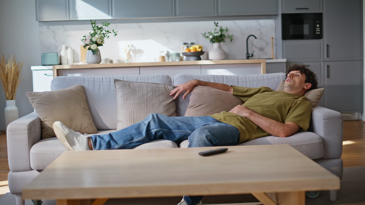 Exhausted brunette falling sofa feeling relaxed at home. Tired man lying couch