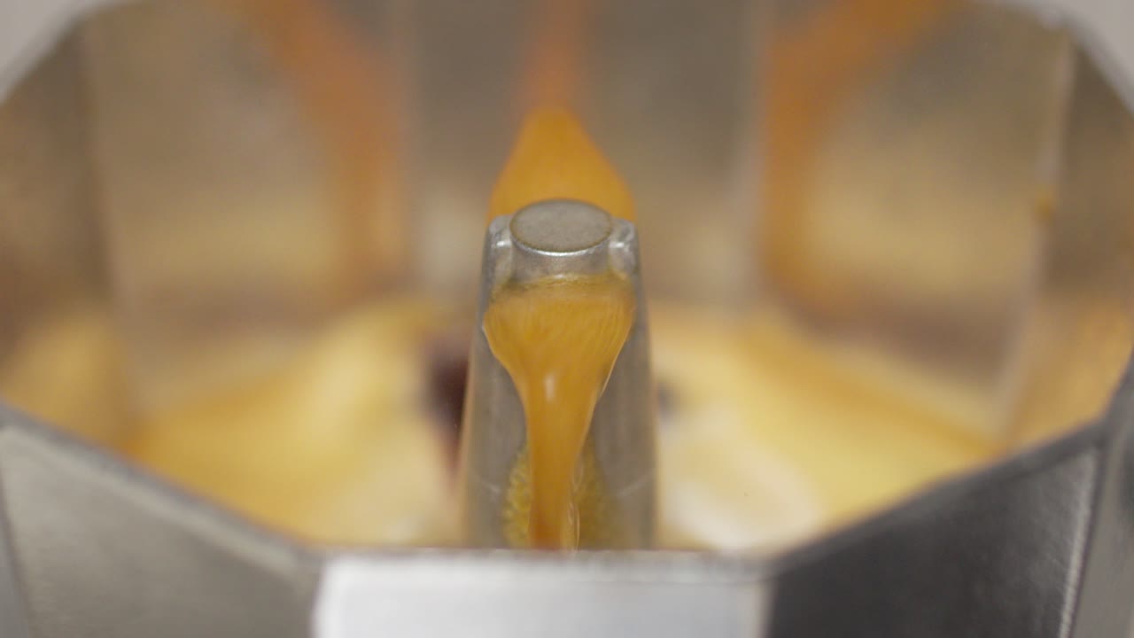 Coffee from a moka pot pours out slowly, showcasing the brewing process in close-up