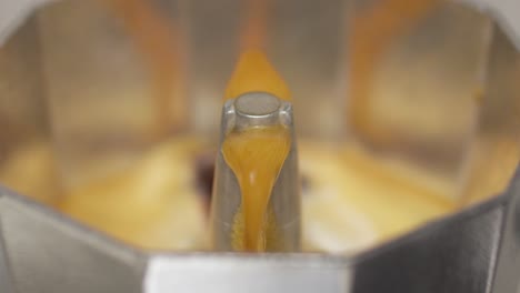coffee from a moka pot pours out slowly, showcasing the brewing process in close-up