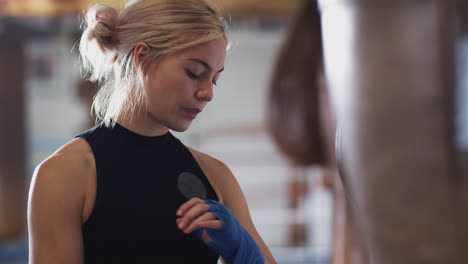 female boxer training in gym putting wraps on hands standing next to punching bag