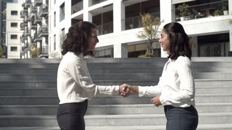 mujeres de negocios felices de pie al aire libre y estrechando la mano
