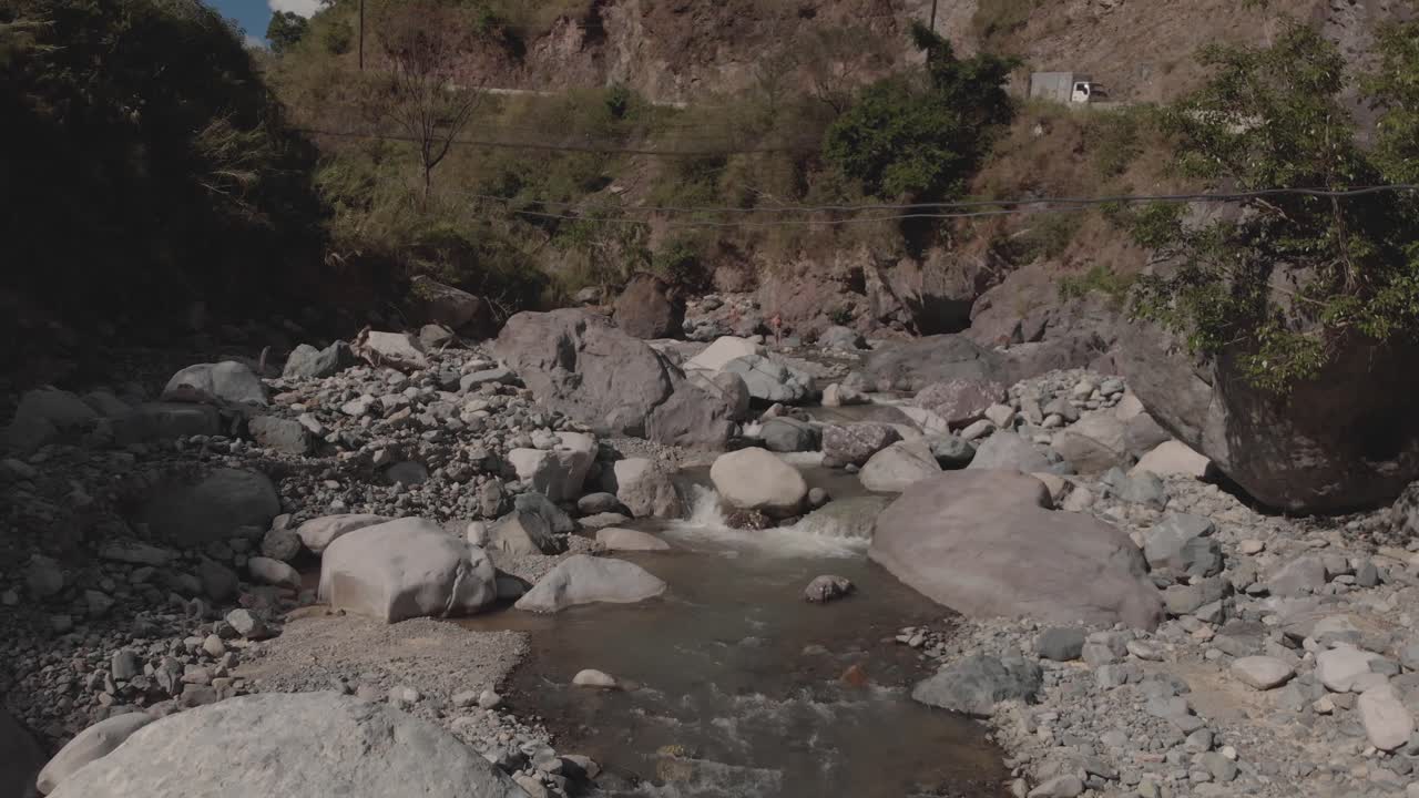 hermoso río rocoso que serpentea a través de las montañas en el valle del cañón agua que fluye acercándose cantos rodados grises árboles verdes cielo azul lento aéreo movimiento suave enfoque sobre el arroyo en cascada naturaleza