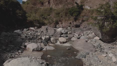 Wunderschöner-Felsiger-Fluss,-Der-Sich-Durch-Berge-Im-Canyon-Tal-Schlängelt,-Fließendes-Wasser,-Das-Sich-Nähert,-Graue-Felsbrocken,-Grüne-Bäume,-Blauer-Himmel,-Langsame-Luftbewegung,-Sanfte-Annäherung-An-Die-Kaskadierende-Bachnatur