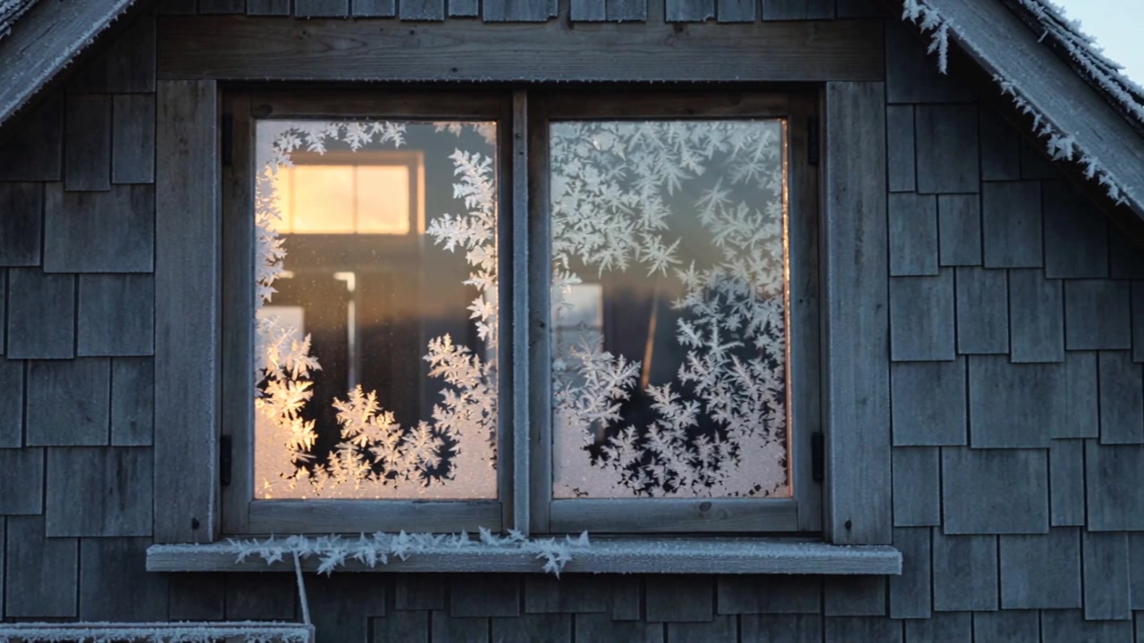 Forming frost crystals spreading across double-pane wooden window on cabin exterior, driven by cold
