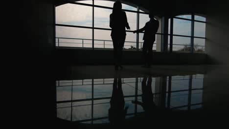 Silhouetten-Von-Zwei-Geschäftsleuten-Treffen-Sich-In-Einer-Geräumigen-Halle-Am-Fenster