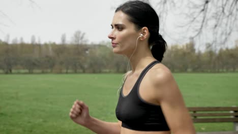 young fit girl is jogging in park in summer, listening to music, healthy lifestyle, sport conception, side view