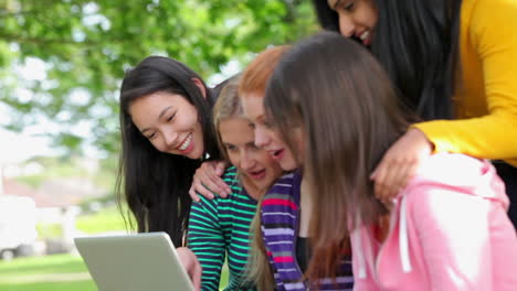 female students looking at the laptop together outside and laughing