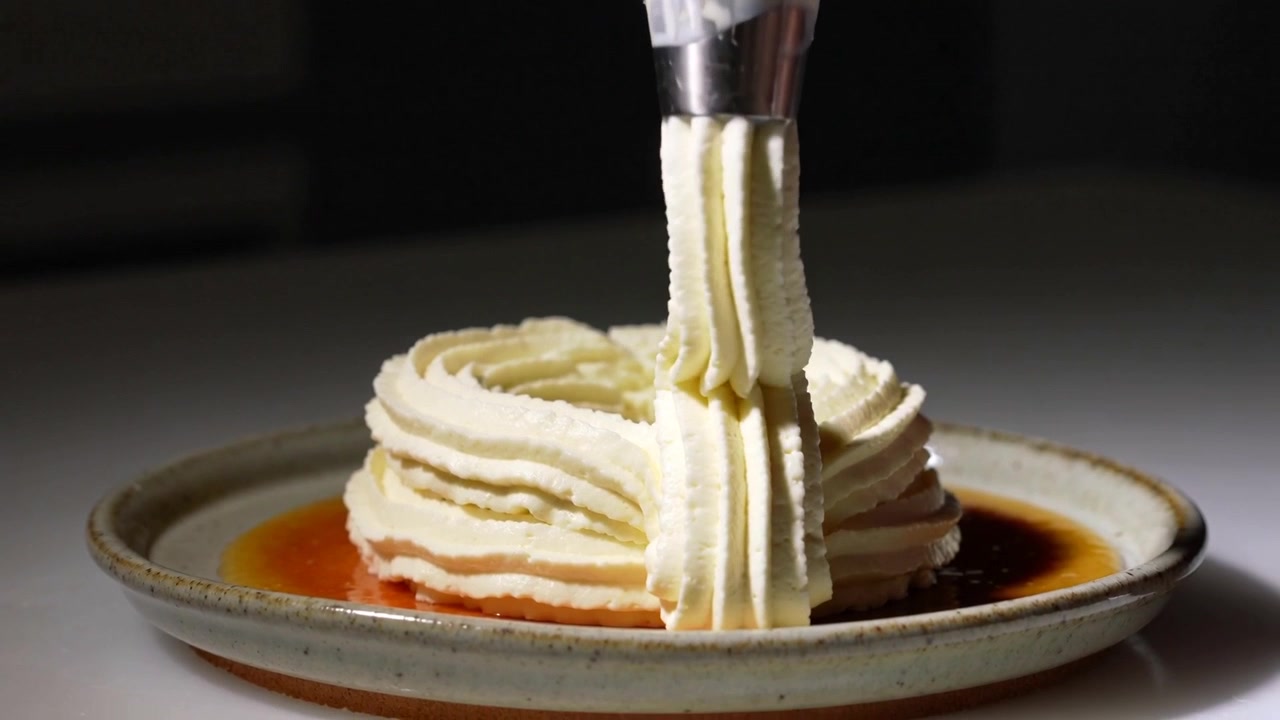 Mão enluvada pressionando apertando o bico do saco de confeitar, decorando anel de creme no balcão com molho âmbar