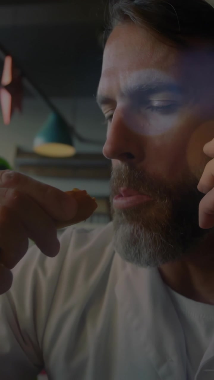 Video verticale: Un uomo riceve una telefonata, tenendo il telefono all'orecchio e addentando un dolce in una caffetteria.
