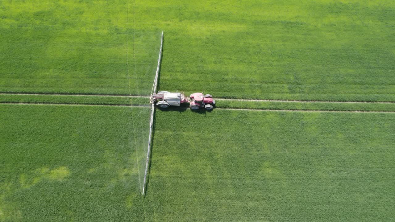 Aerial trucking shot of the agricultural sprayer spraying insecticide to the green field agricultural works on spring