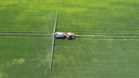 toma aérea de camiones del rociador agrícola rociando insecticida a los trabajos agrícolas de campo verde en primavera
