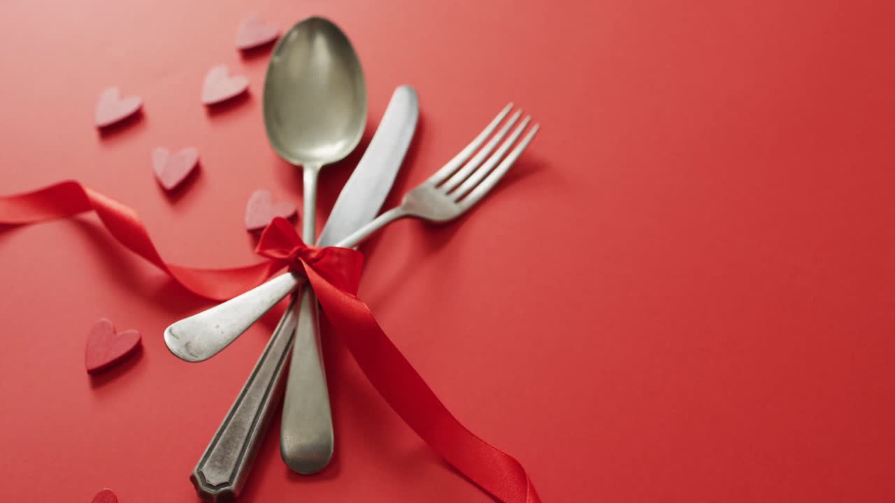 Red ribbon and cutlery with hearts on red background at valentine's day