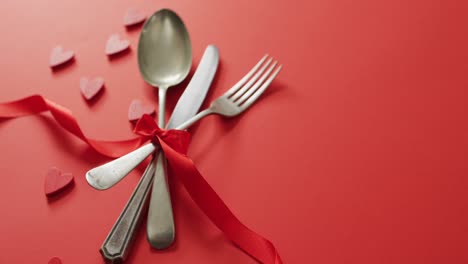 red ribbon and cutlery with hearts on red background at valentine's day