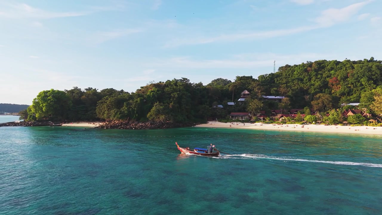 Impresionante vista aérea cinematográfica, un barco tradicional de cola larga navegando por una bahía tropical cerca de las Islas Phi Phi, Krabi, Tailandia, con agua turquesa, playa de arena y exuberante paisaje isleño.