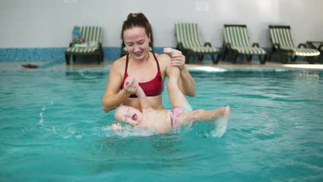 Happy-smiling-little-kid-is-swimming-together-with-his-mother-in-the-swimming-pool.-Young-mother-is-spinning-and-whirling-him-around-having-fun-together