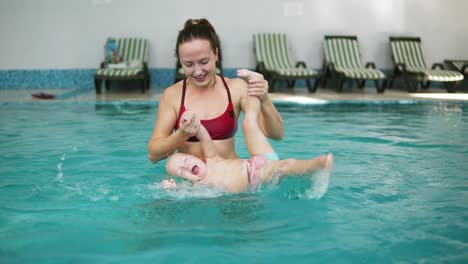 un niño sonriente feliz está nadando junto con su madre en la piscina. la madre joven está girando y girando alrededor de él divirtiéndose juntos