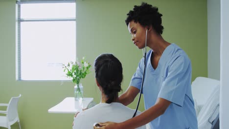 side view of african american female doctor examining female patient in the ward at hospital