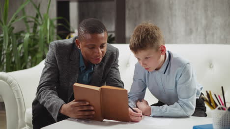 black tutor reads book with schoolboy studying english