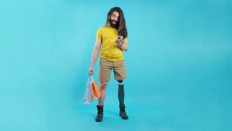 smiling man with prosthetic leg holding shopping bags and using phone