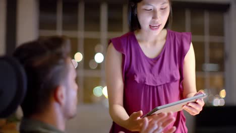 focused diverse male and female colleague discussing work and using tablet at night in office