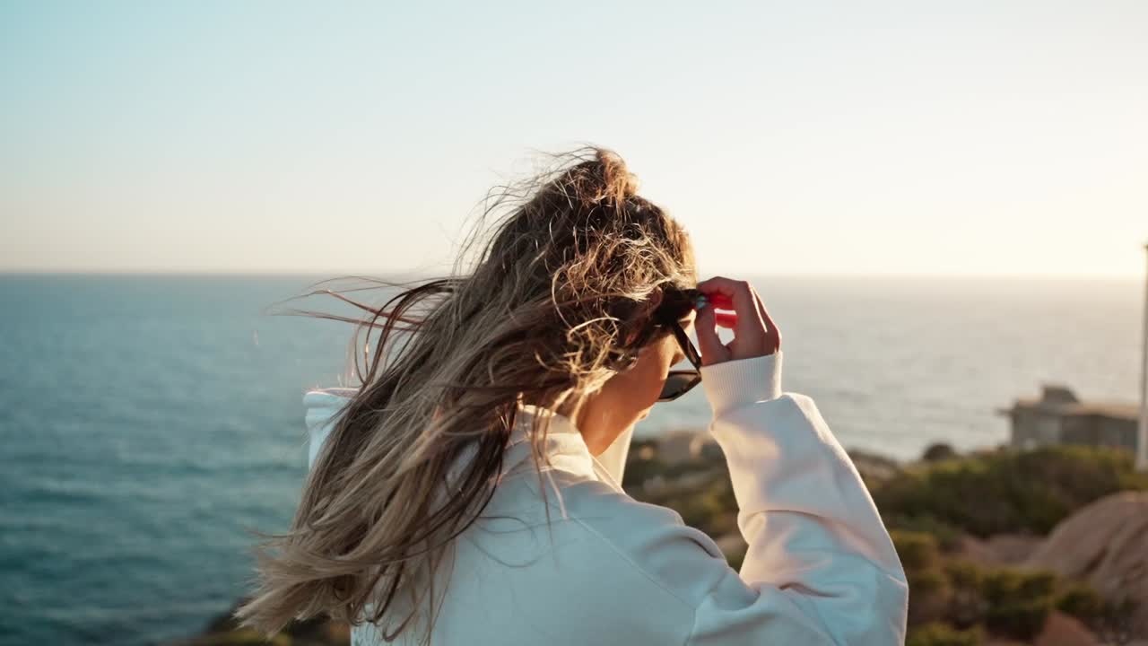 Approaching a free spirit girl enjoying sunset from seaside rocks