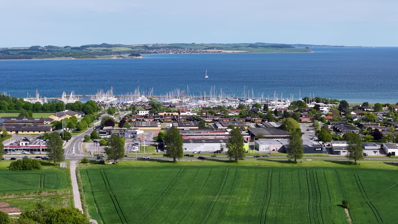 Aerial drone view of a coastal town with green fields in the foreground and a harbor full of boats along the shoreline