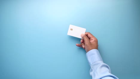 hand holding a white credit card on a light blue background