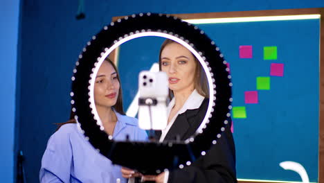 two caucasian ladies stand behind the camera with light ring. recording content for modern blog.