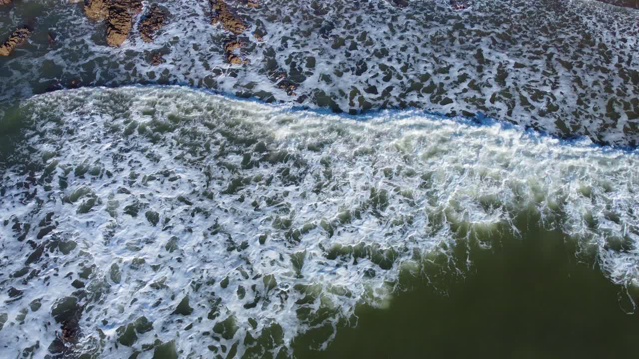 Top Down Aerial View of Sea Waves Rolling Over Beach Rocks Under Bright Sunshine