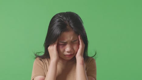 close up of young asian woman victim of violence with bruise on face being stressed and having a headache in the green screen background studio