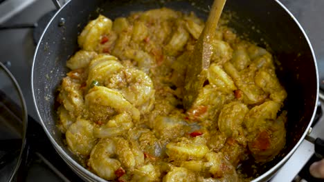 una persona usa un palo de madera para agitar el curry de camarón, ofreciendo una vista de cerca de la deliciosa comida en un plato, encarnando el concepto de experiencia culinaria