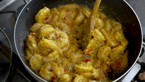 a person uses a wooden stick to stir prawn curry, offering a close-up view of the delicious meal in a dish, embodying the concept of culinary expertise