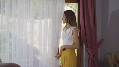 en casa, la mujer que mira por la ventana se sienta en el sillón.