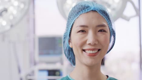 video portrait of smiling asian female surgeon wearing surgical cap in operating theatre, copy space