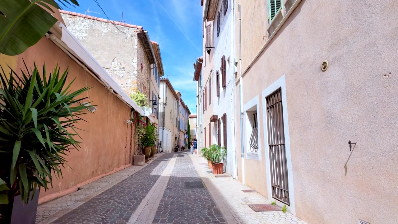 Una ripresa in movimento dal basso si muove attraverso uno stretto vicolo mediterraneo con edifici colorati e piante.